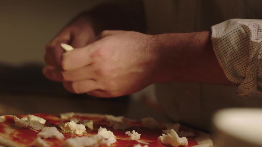 Closeup of a mans hands putting ingredients on a pizza