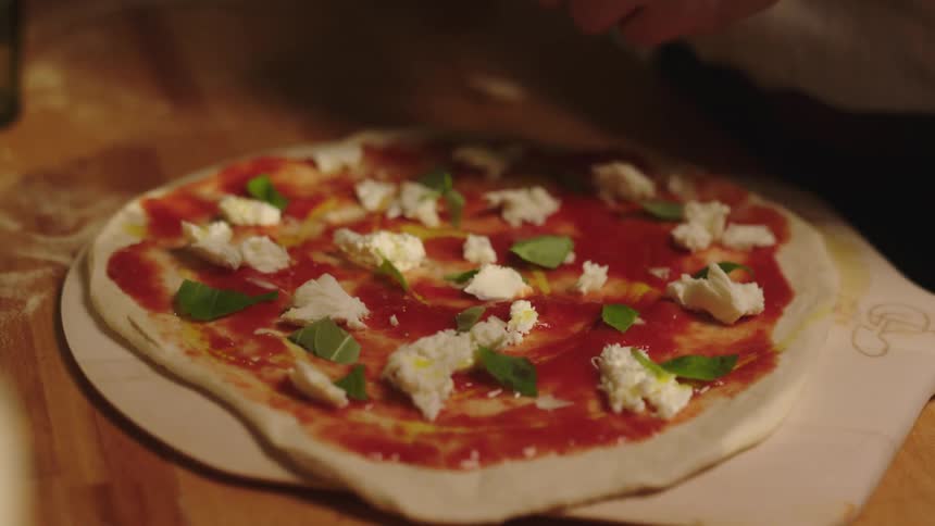 Hands of a man putting vegetables on pizza inside the kitchen