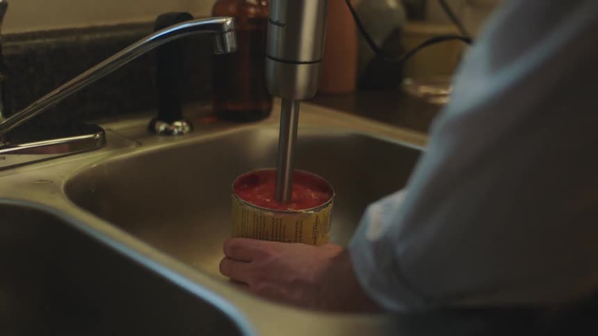 Man mixing a can of tomatoes on the kitchen sink