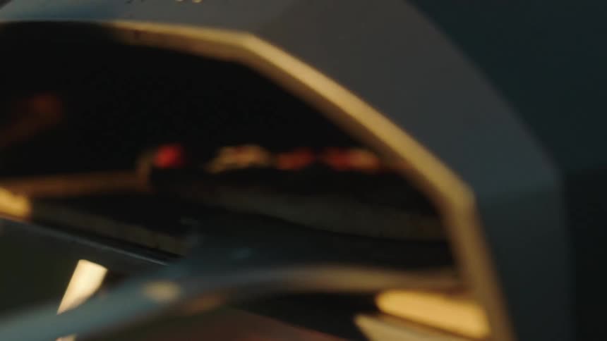 A utensil placing a pizza in an oven and it starts to bake