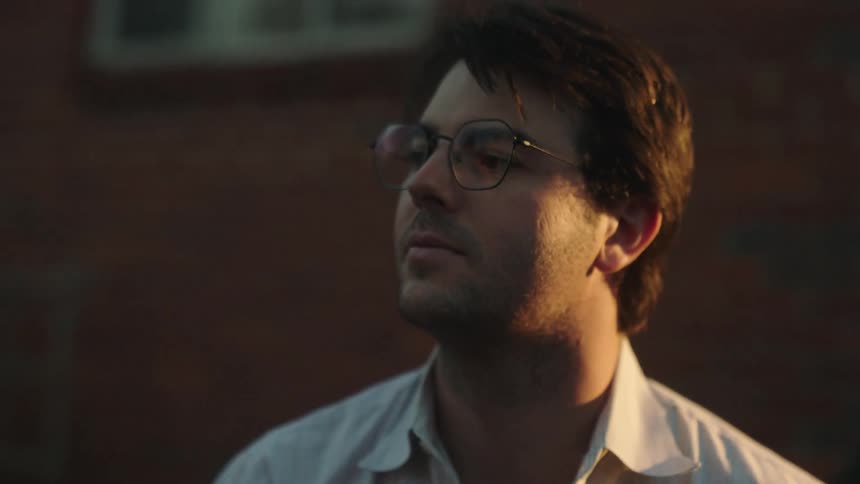 Dark haired man with glasses leans forward outdoors