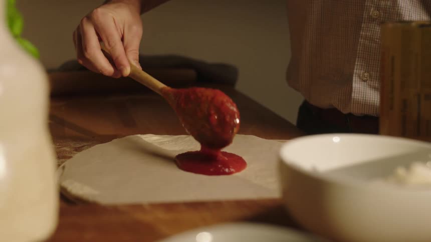 A man spreading tomato sauce over dough to make pizza