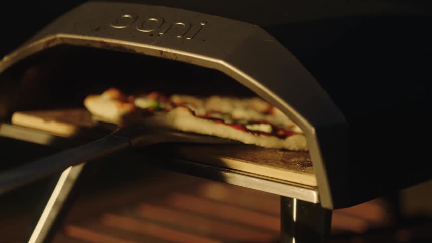 Close up of a person moving a pizza inside an oven