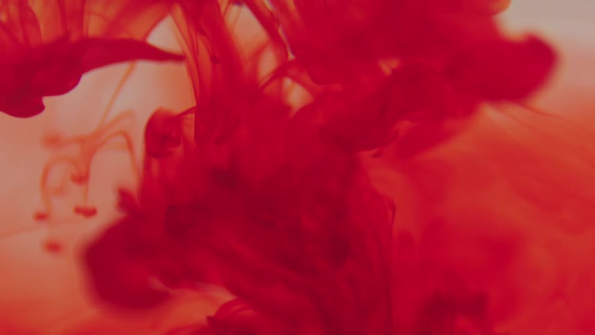 Red inky dye dropping into clear liquid spreading into ribbons and fading in color