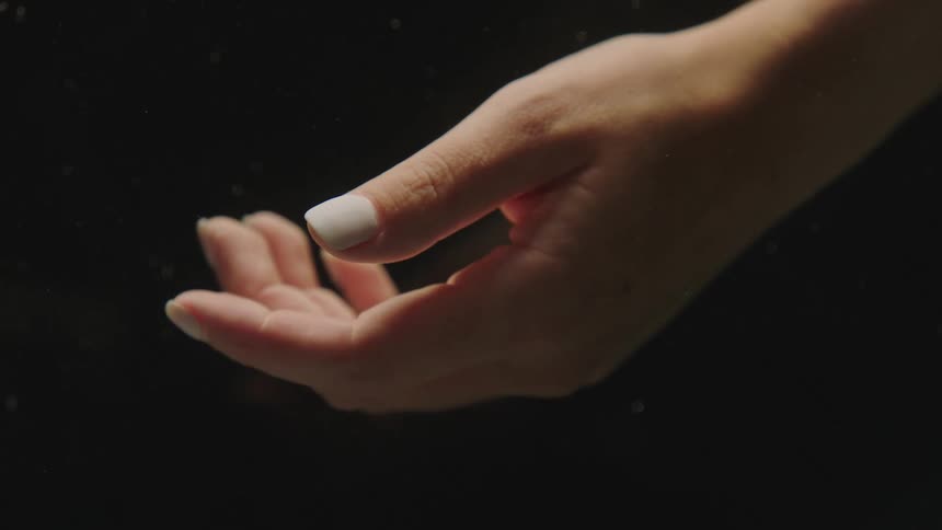 Close up of feminine hand with pale polished fingernails against a dark background
