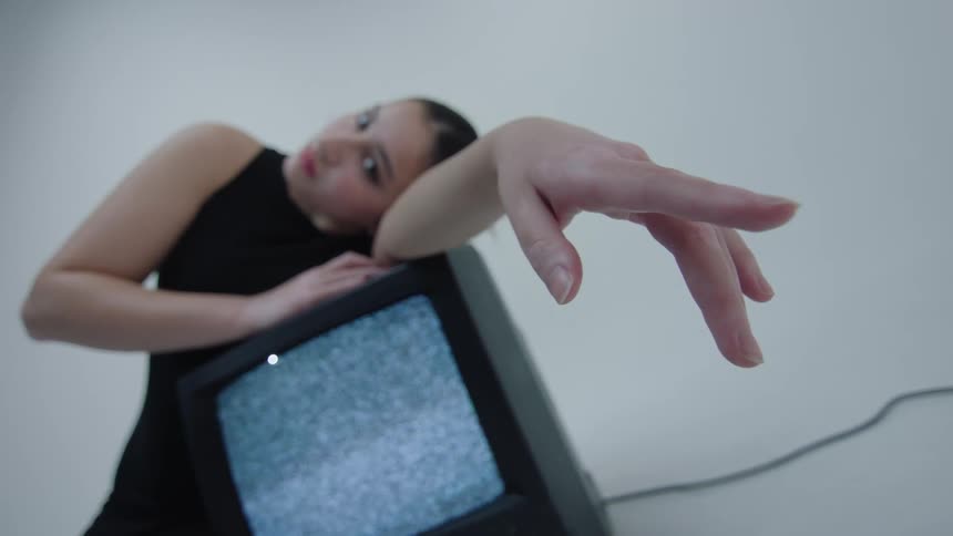 Model in a studio posing with the body under a television with no signal turned on