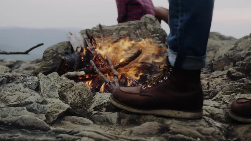Closeup of a small campfire amid rocks with people around