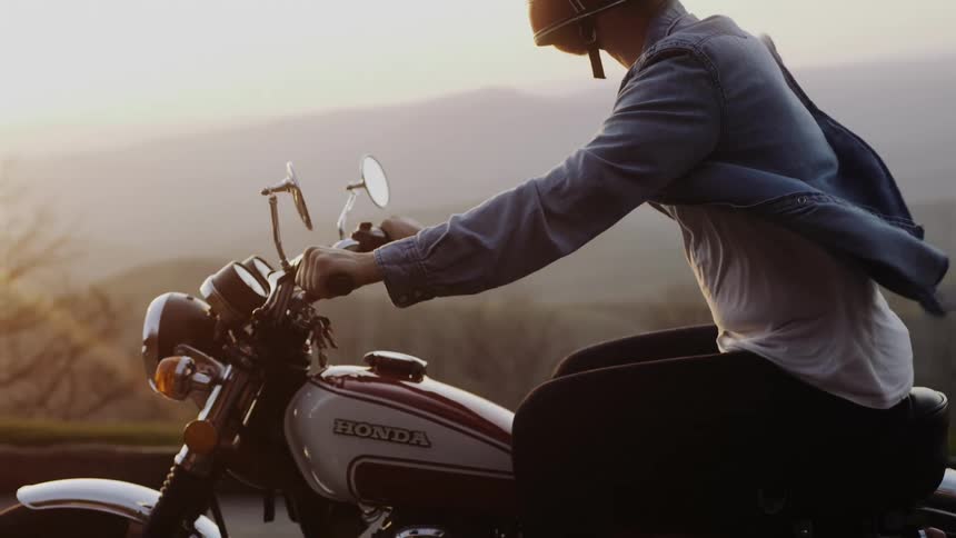 A person wearing a helmet riding a motorcycle and his coat flies in the wind