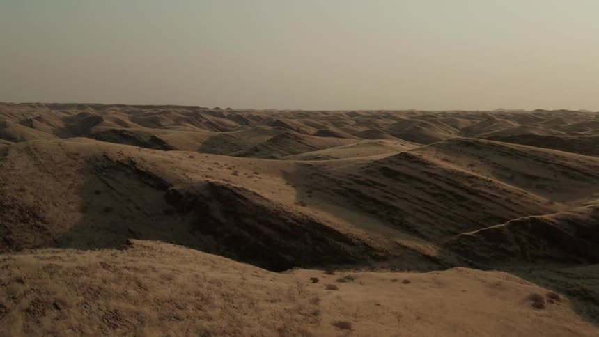Brown sand dune hills in the desert touching a hazy sky