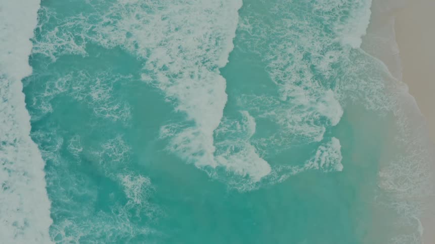 Aerial view of ocean waves breaking against the sandy beach