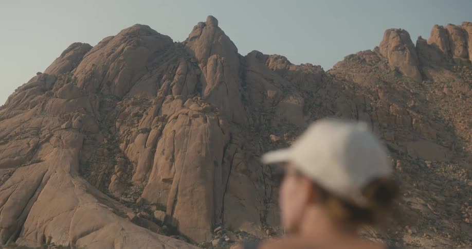 Woman wearing a white cap watches rocky mountain