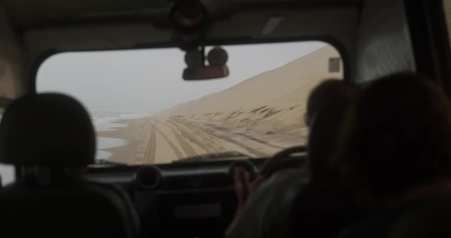 View from inside the car of the driver driving on the sandy beach next to the sea on a cloudy day