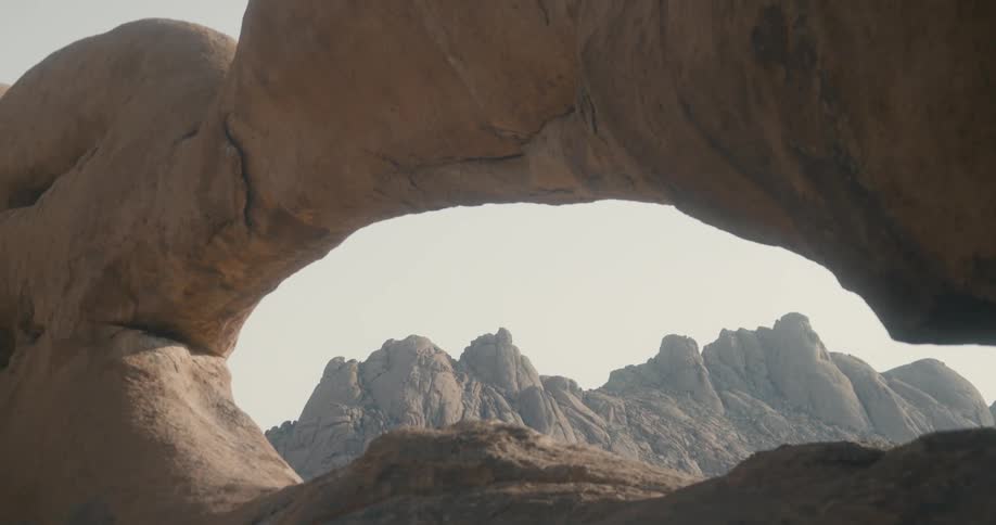 Arch shaped rock formation with a hazy daytime sky and rocky plateaus in the background