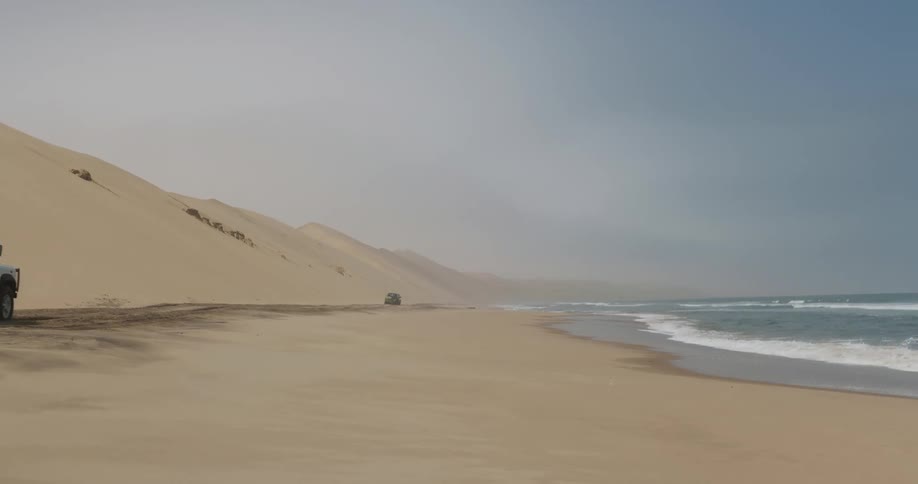 Vehicles drive along beach at the base of sand dune