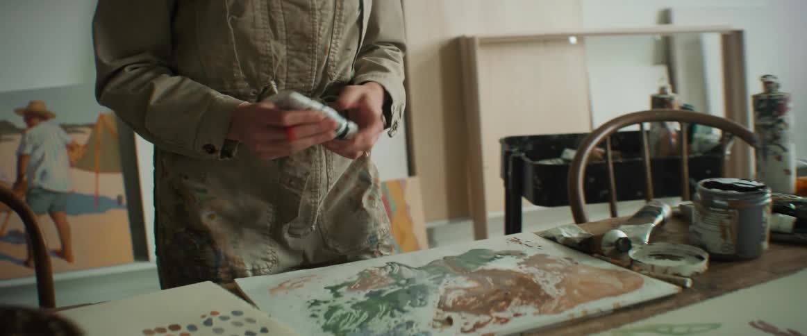 Closeup of a painters hands putting paint on a canvas and holding a brush