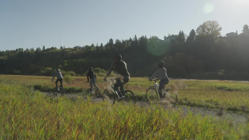 Family with two children all riding bicycles on a narrow road through a grassy landscape on a day with a blue sky and no clouds