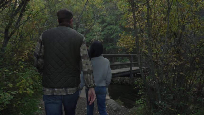 Family walking in a nature park towards a wooden bridge over a lake