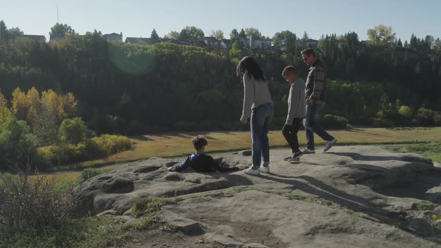 Family looks down at boy sitting in hole on hill across road from residences on an opposite hill
