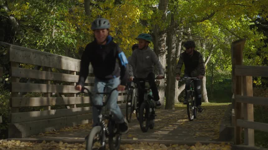 A family of four riding a bike over a wooden bridge