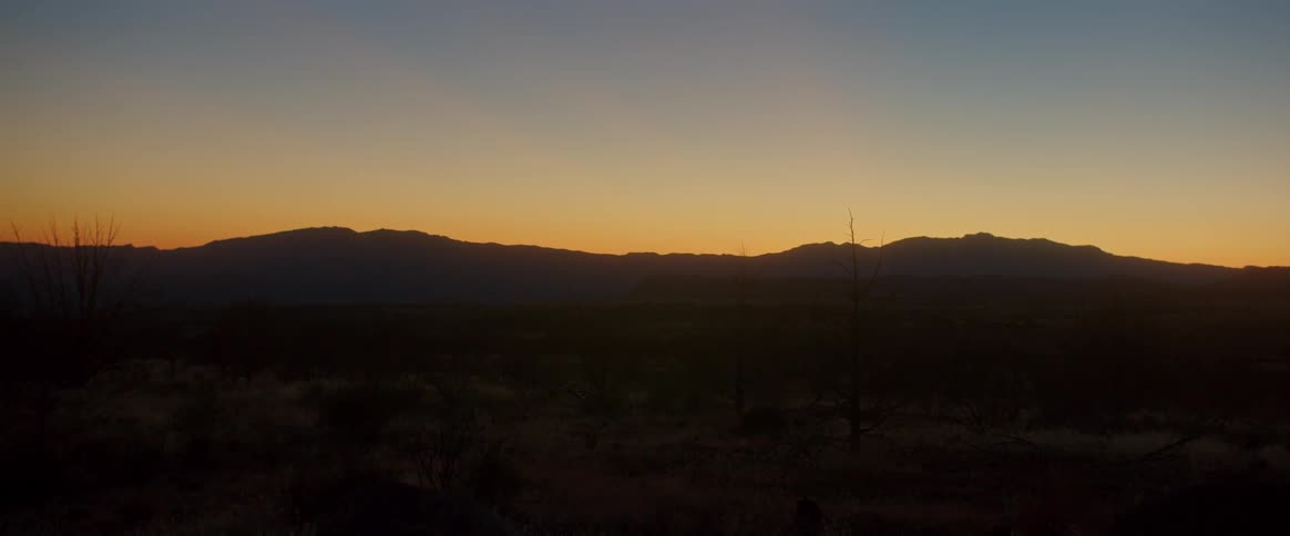 Panorama of a landscape with the silhouette of a mountain range and the sun rising on the horizon