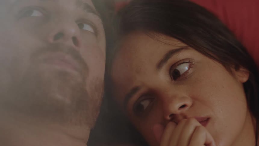 A woman looks up at a man while they lay together