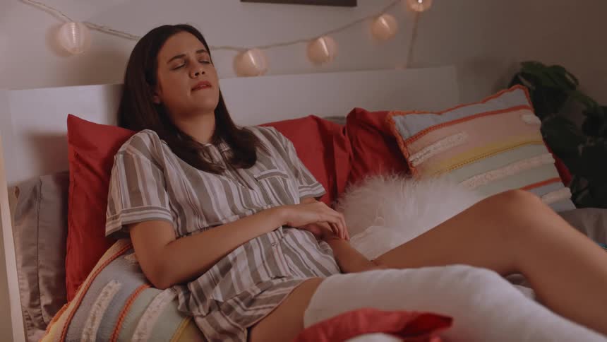 Woman lying in bed with one of her legs in a cast waking up and trying to reach for something without getting out of bed