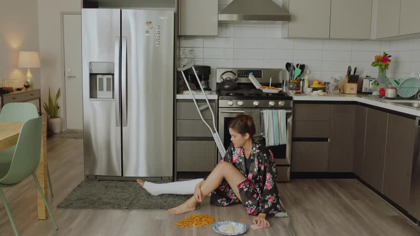 A woman with a broken feet with casting is picking food from the floor