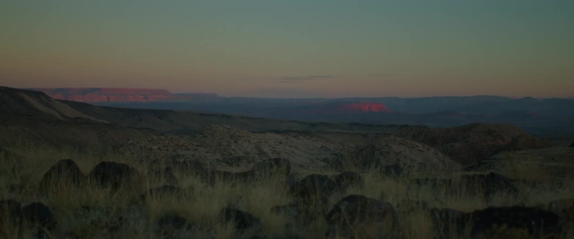 A landscape of a region with some small mountains in the morning and an orange sky
