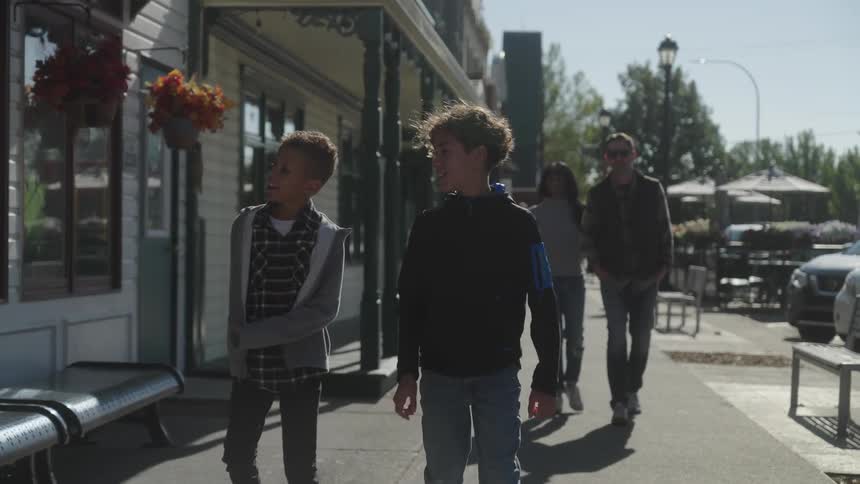 Two teens and two adults walk on along a sidewalk lined with small shops
