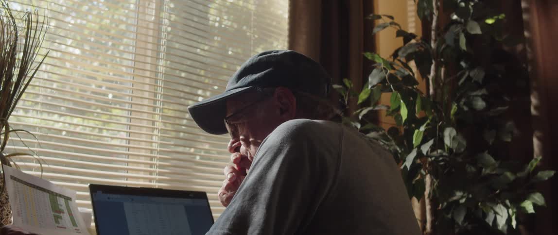 A man is reading a paper and looking at his laptop