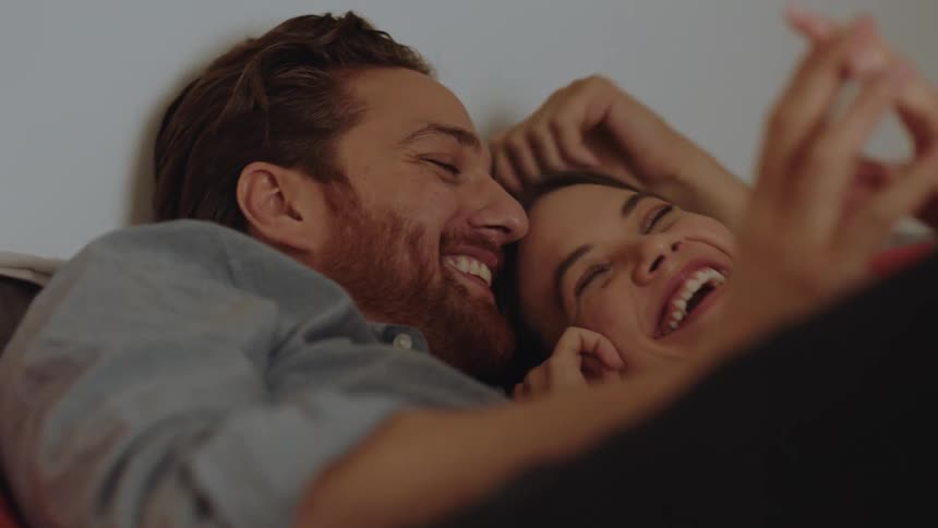 Young happy couple talk and laugh in bed