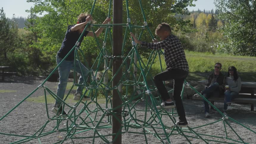 Parents watch two children climb in the playground