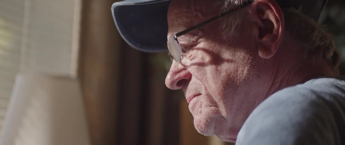 An elderly man puts on eyeglasses and starts reading something