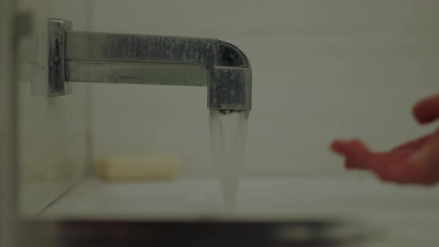 An adult hand touches running water in a bathtub