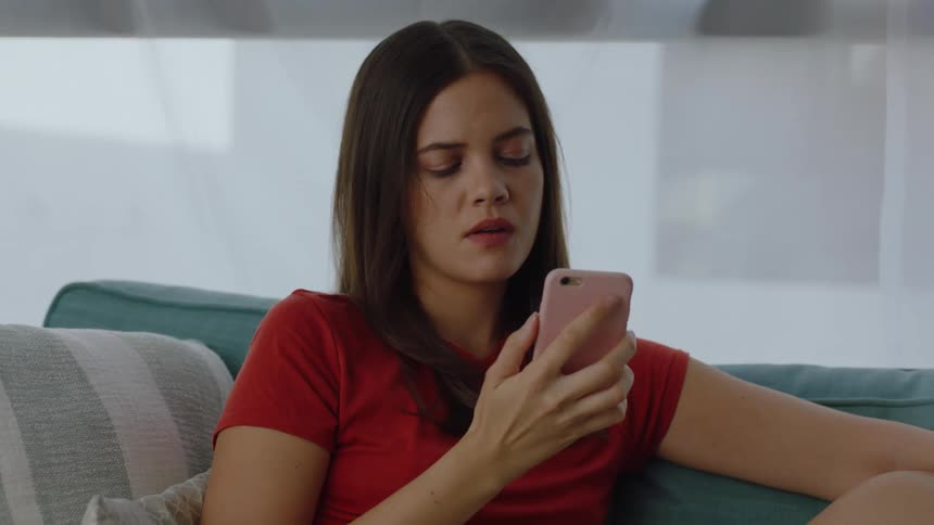 Woman sitting on the couch answering the phone and hanging up with a facial expression of sadness