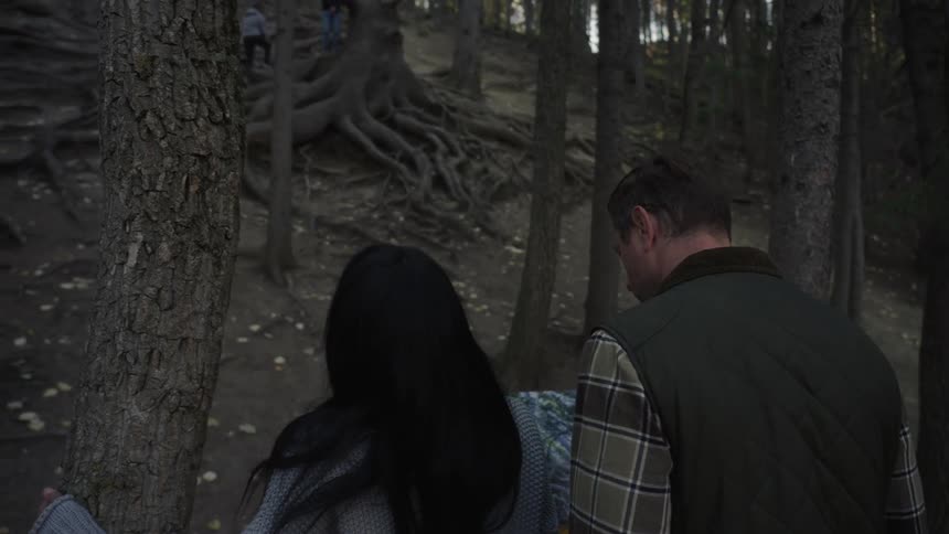 Parents looking at a sign while their children are playing among the roots of a tree in a park with abundant vegetation