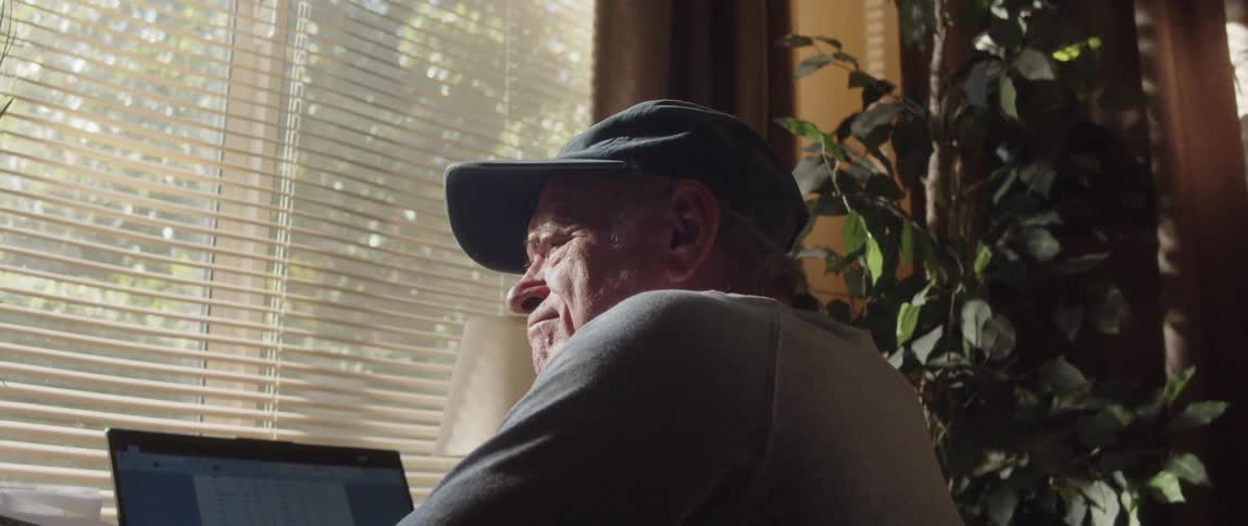 Elderly man sitting in front of computer takes off glasses and thinks