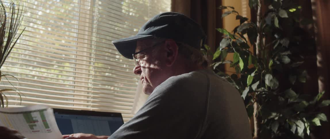 Elderly man goes through letters and compares them to information on computer screen while sitting at home