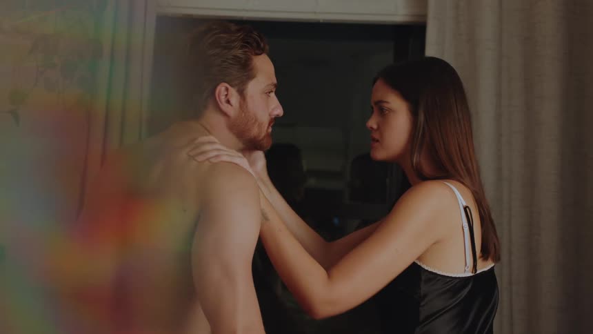 Woman wearing lingerie stares into mans face and both caresses and shakes him