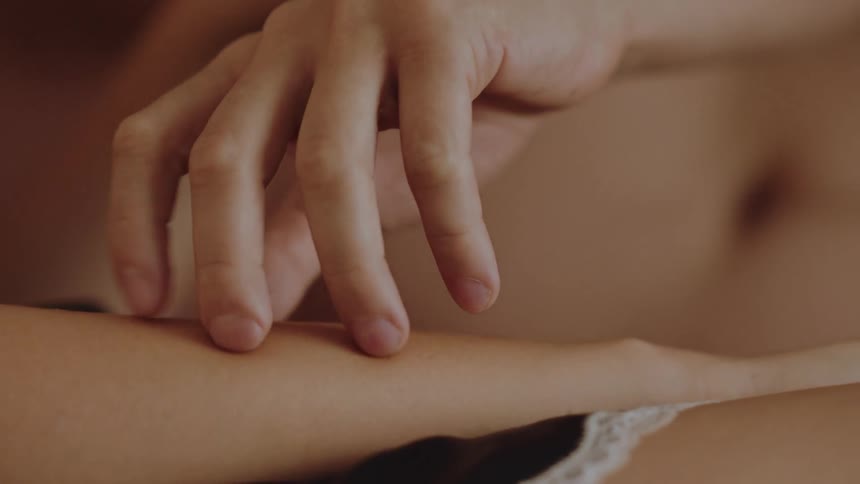 A mans hand uses his finger tips to caress the arm of the woman in bed next to him