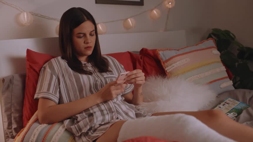 Woman lying in bed using her cellphone with one of her legs cast and bandaged