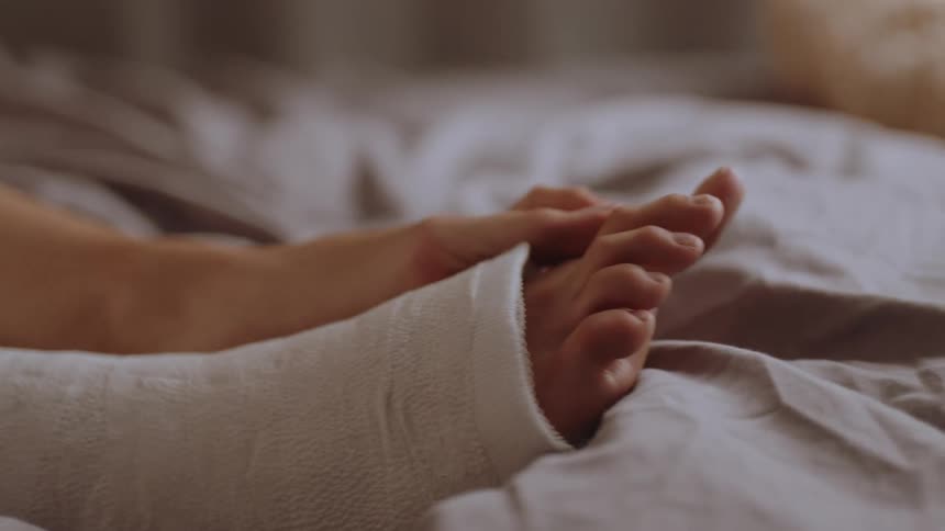 Legs of a woman lying in bed with one of them in a cast