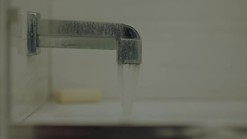 A metal faucet is open and water is pouring into the sink