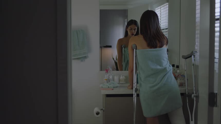 Woman in crutches brushes her teeth in the bathroom