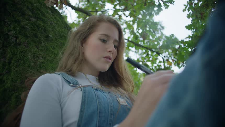 Young blonde woman reclined on a tree writting