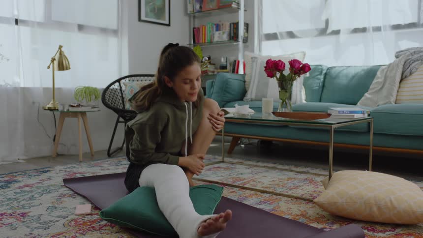 Woman with a cast on her leg stretches on the floor