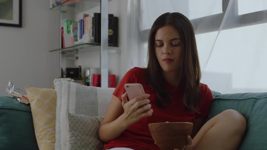 Woman eating popcorn at home checks her phone