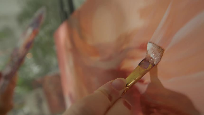 Closeup of a painters hands holding a brush and painting a canvas