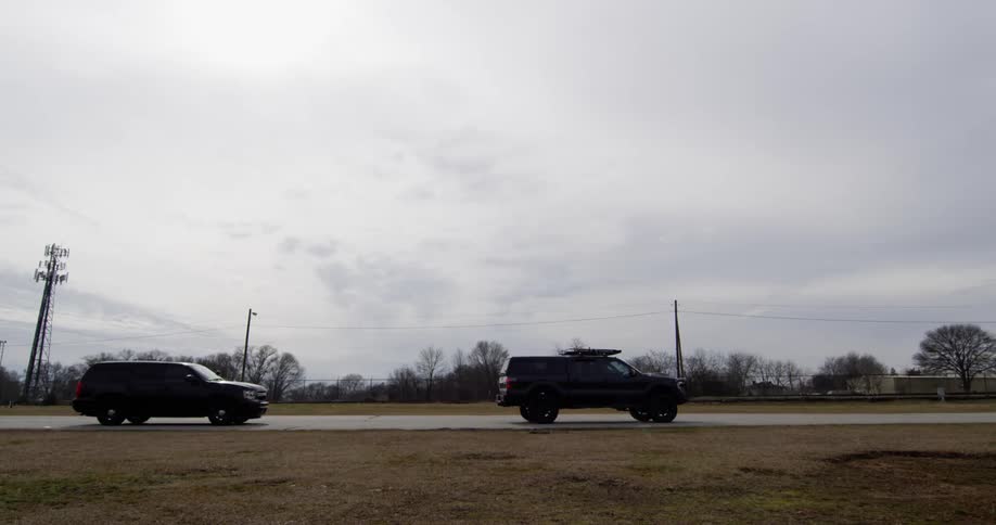 Four vehicles drive on road near barren trees during the day