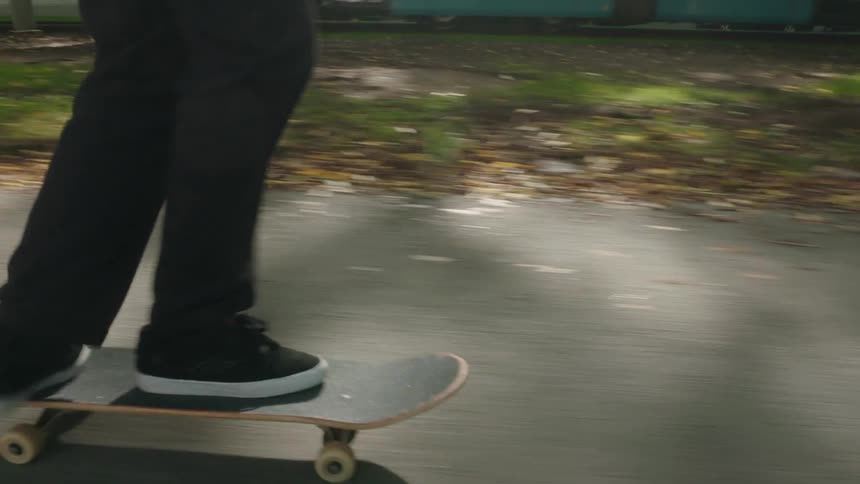 Man with long curly hair beard green jacket and jeans skateboards on road next to tram running on rails along the street